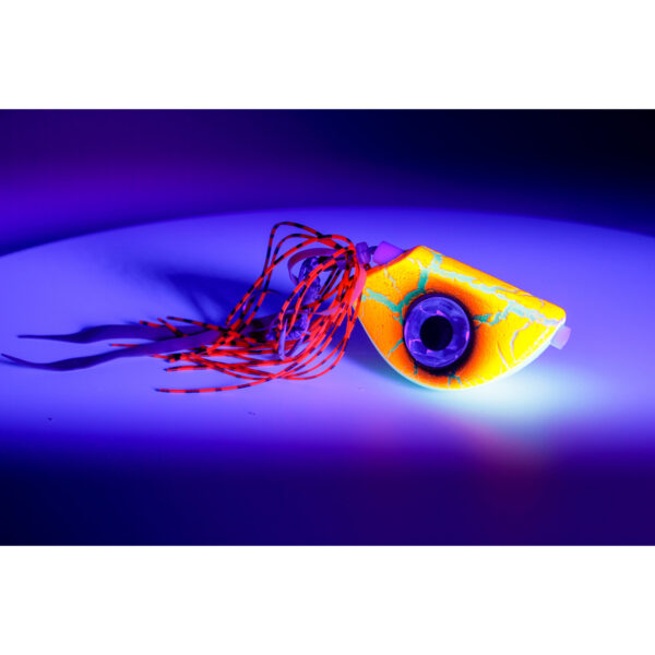 Beneath the glow of purple light, the Catch Beady Eye Kabura Jig stands out with its vibrant yellow body, enhanced by a beady eye and striking red tassels. Its intricate design is truly a sight to behold.